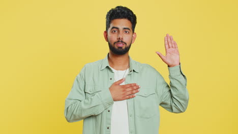 Indian-man-raising-hand-to-take-oath,-promising-to-be-honest-and-to-tell-truth-keeping-hand-on-chest