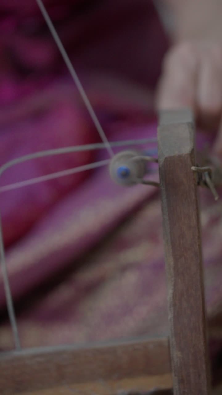 Close up slow motion of a hand adjusting silk thread on a traditional winding mechanism in a local weaving silk fabric textile workshop vertical format