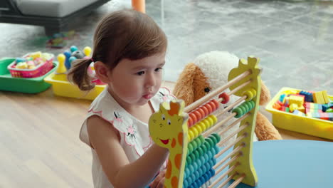 toddler girl study calculation by moving colorful beads on rods of educational kid's abacus inside playroom