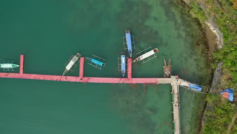 overhead ascending aerial view of philippine banca boats docked in tropical aqua blue water beside an island in 4k