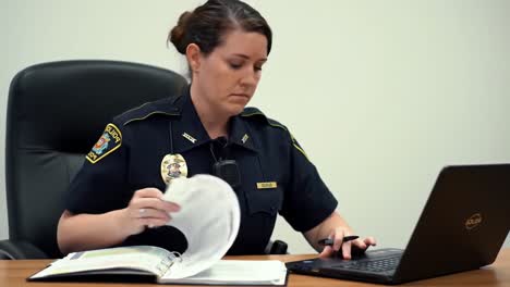 a focused law enforcement officer diligently reviews reports and enters data into her laptop, showcasing the important responsibilities of modern policing in a professional setting