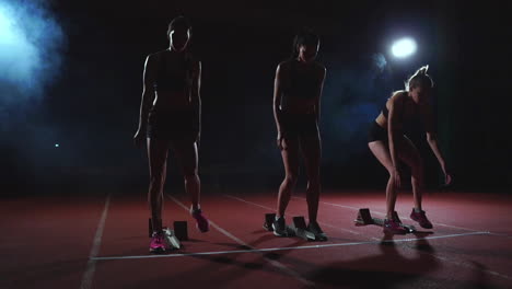 female runners at athletics track crouching at the starting blocks before a race. in slow motion.