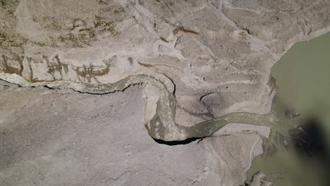 Small-water-stream-flowing-through-the-mountains-into-the-glacier-lake,-Slow-motion,-Drone-shot