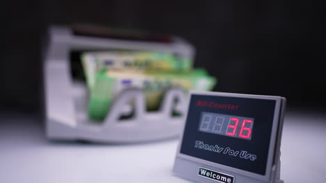 starting a modern automatic cash counting machine. red numbers change on the display. light green banknotes are counted in equipment at blurred backdrop.