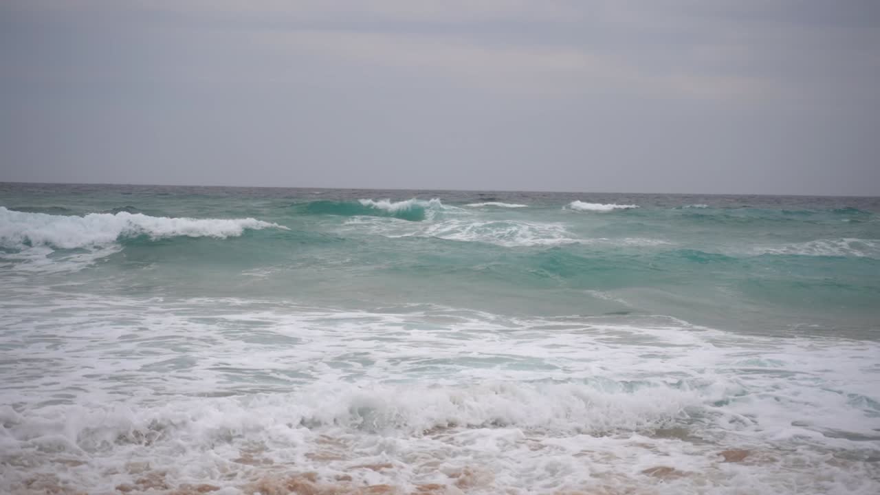 바다의 파도가 흐리고 바람이 불는 날 오스트레일리아의 해안으로 굴러오고 있습니다.