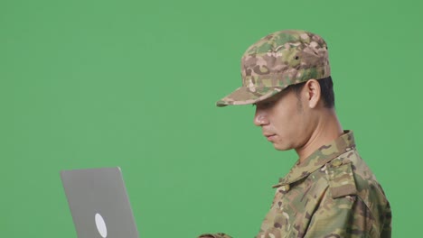 un soldado asiático usando una computadora portátil mientras camina en el estudio de fondo de la pantalla verde