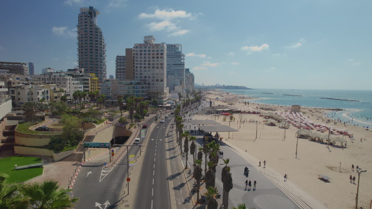 Push in drone shot above Gordon promenade tel aviv and Frishman beach full of visitors on a warm and calm summer day - the promenade It's also a jogging track for many people