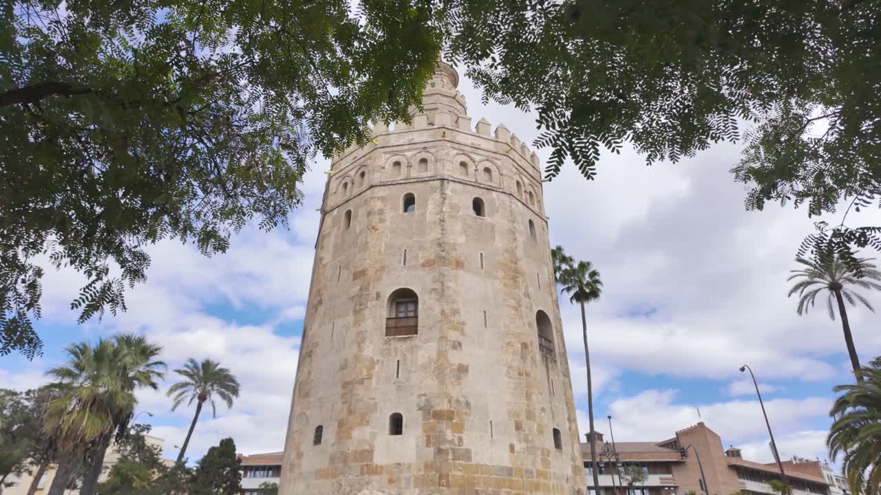Torre del Oro in Seville, Spain, with palm trees and a dramatic sky overhead