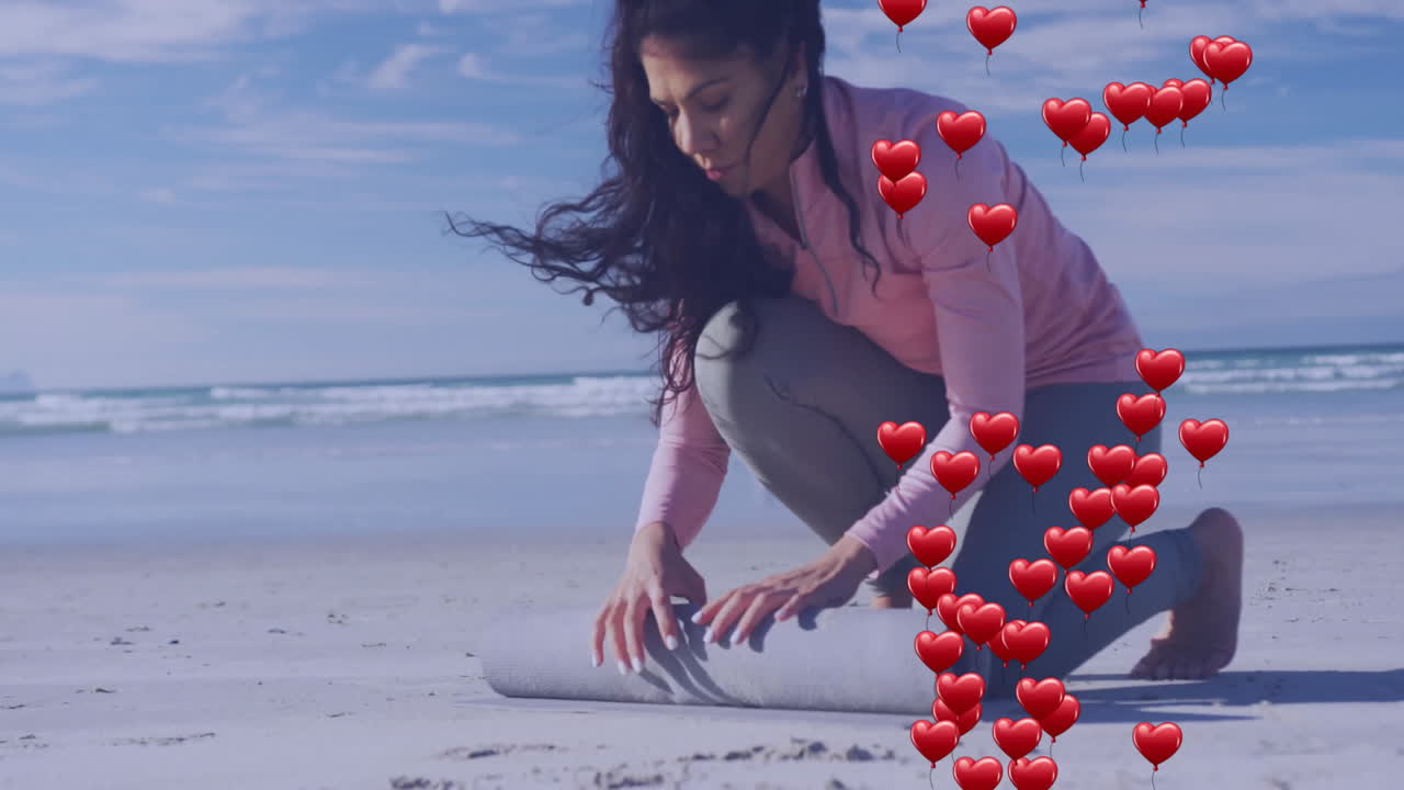 Rolling mat on beach, woman with heart animation overlay, preparing for exercise