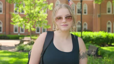 girl student wearing sunglasses stands in from of a college university