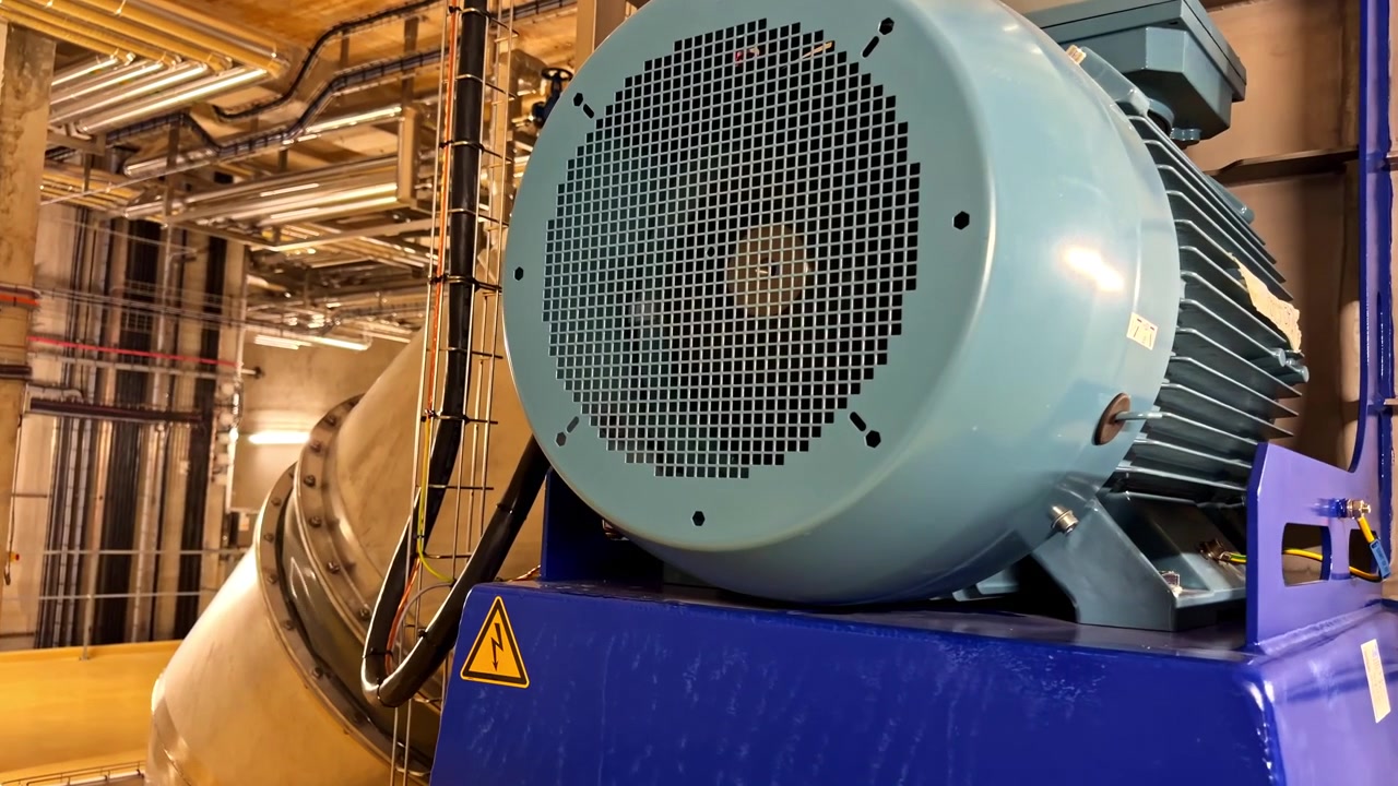 Un grande motore blu spicca in un impianto energetico, circondato da tubazioni metalliche. Ideale per contenuti di ingegneria e industriali.