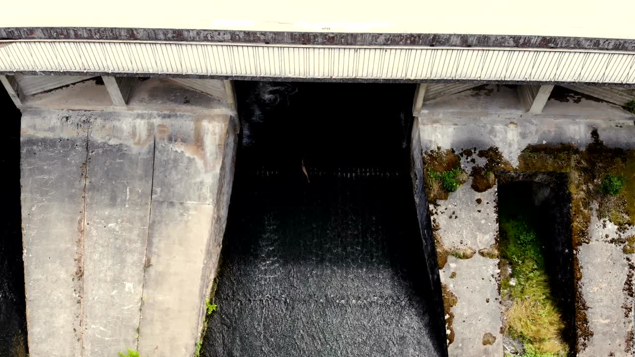 Aerial view of water rushing through the gates at a dam and bridge