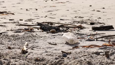 Nahaufnahme-Einer-Plastikflasche-Inmitten-Von-Trümmern-An-Einem-Sandstrand,-Die-Auf-Die-Umweltverschmutzung-Hinweist