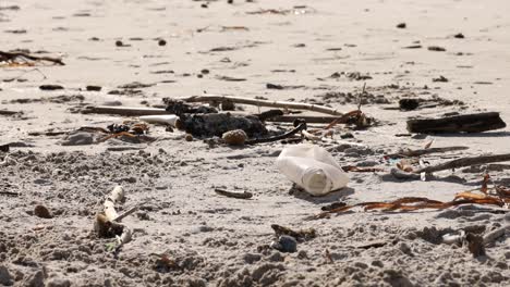 close-up of a plastic bottle amidst debris on a sandy beach, highlighting pollution