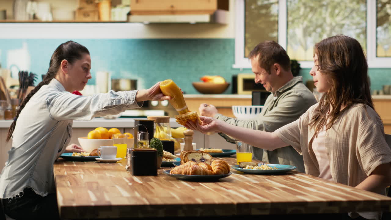 Family sitting around breakfast table and serving meal with pastry and waffles