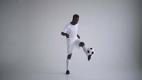 a professional black football player in a white uniform on a white background juggles a ball in slow motion. african-american ethnic group soccer player with a soccer ball