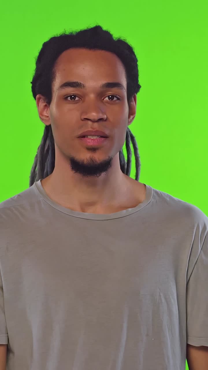 Person med dreadlocks gestikulerer for stilhed foran en grøn skærm.