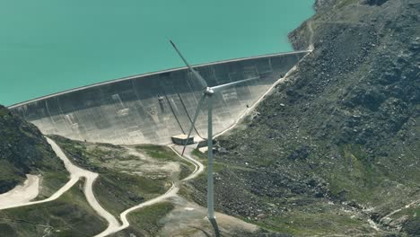 Wind-power-windmill,-spinning-next-to-a-water-dam-in-grimselpass,-switzerland