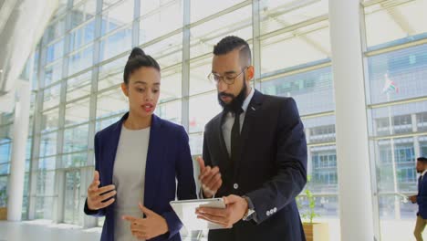 Mixed-race-business-people-discussing-over-digital-tablet-in-the-lobby-at-office-4k