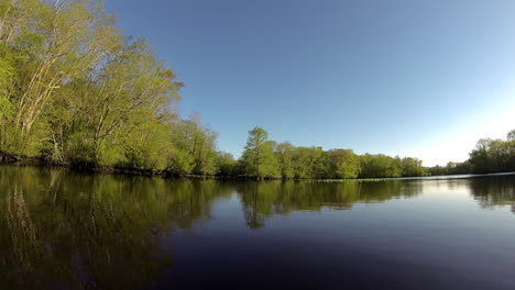 boat-mounted forward trucking shot advances through glassy still water. wooded shoreline is mirrored in water.