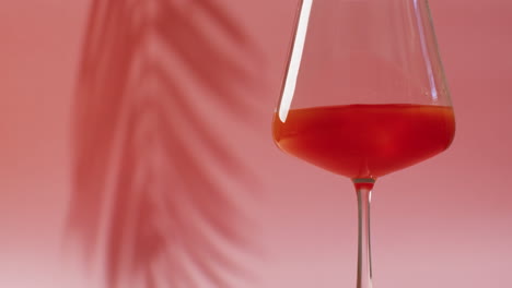cerca de la bebida en un vaso con sombra de hoja en fondo rosa.