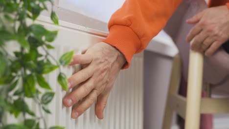 the man warms his hands on the heating radiator by the wall.