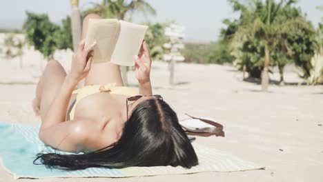 Hispanische-Frau-Mit-Sonnenbrille,-Die-Auf-Dem-Rücken-Am-Strand-Liegt-Und-Buch-Liest,-Kopierraum,-Zeitlupe