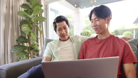 using laptop, asian father and son sitting on couch, bonding and smiling together