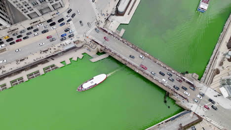 aerial view rotating above a ferry driving under the franklin–orleans street bridge, in green dyed waters of the chicago river