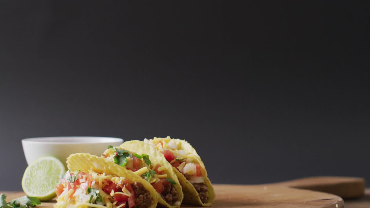Video di tacos appena preparati e ciotola con salsa adagiati su tagliere su sfondo grigio.
