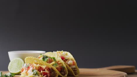 Video-of-freshly-prepared-tacos-and-bowl-with-sauce-lying-on-board-on-grey-background