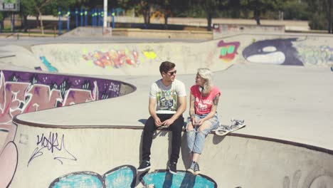 Young-couple-sitting-on-a-wall-at-a-skate-park