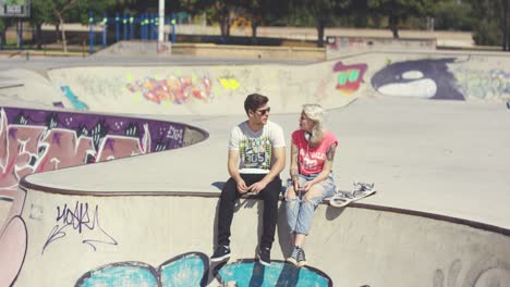 Pareja-Joven-Sentada-En-Una-Pared-En-Un-Parque-De-Skate