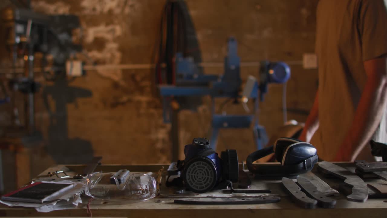 Midsection of caucasian male blacksmith walking in workshop with tools on table