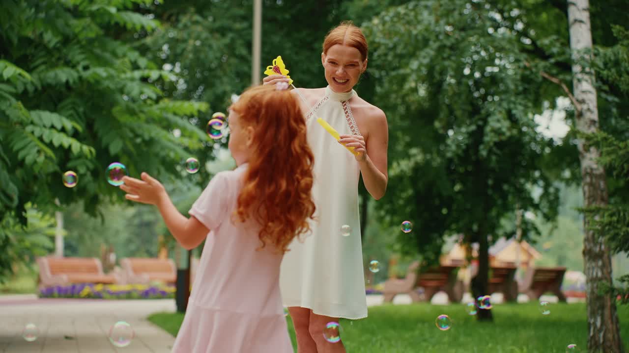 мать и дочь играют с пузырьками в парке