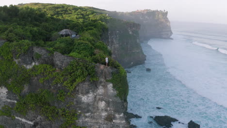 man stands at steep cliff edge overlooking ocean