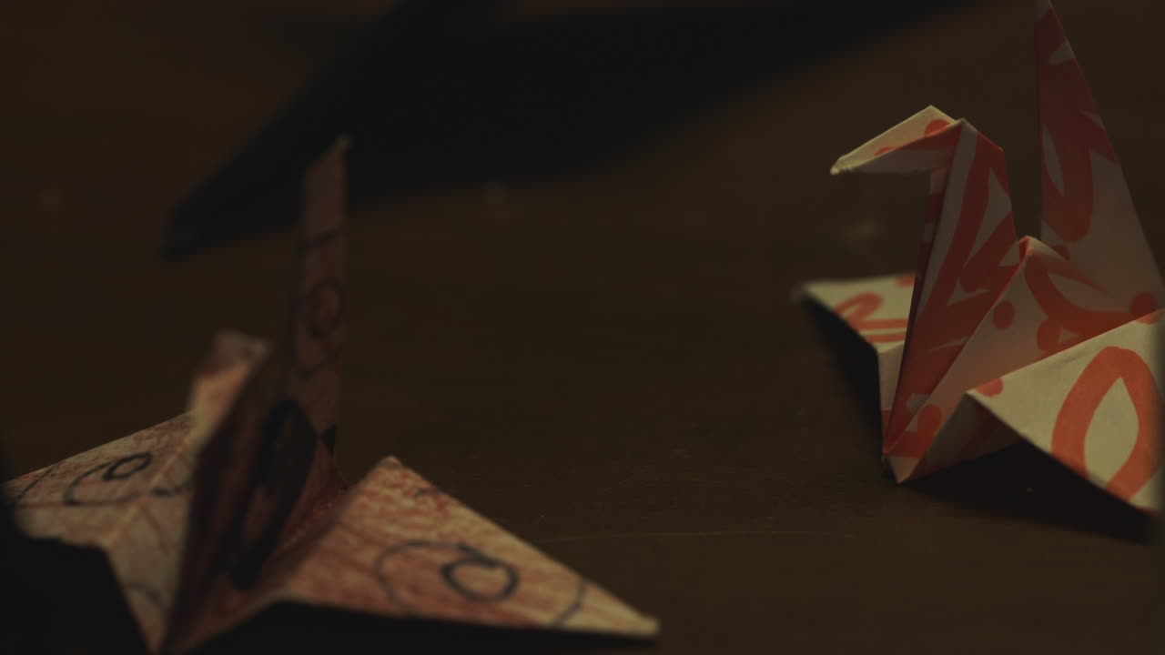 Hand Places Origami Bird Down on Table in Dark Room, Panning Down
