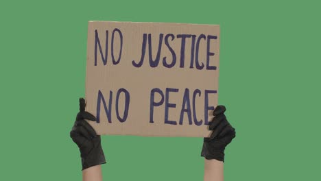 no justice no peace. protest text message on cardboard. stop racism. police violence. banner design concept. hands in black gloves holding a poster a green screen, chroma key. close up. slow motion