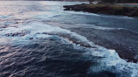 water forming white froth as tide rolls into remote bay at sunset, aerial