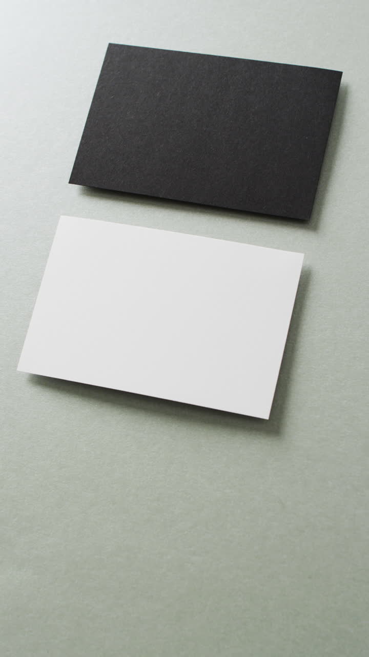 Vertical video of black and white business card arranged on grey background, copy space, slow motion