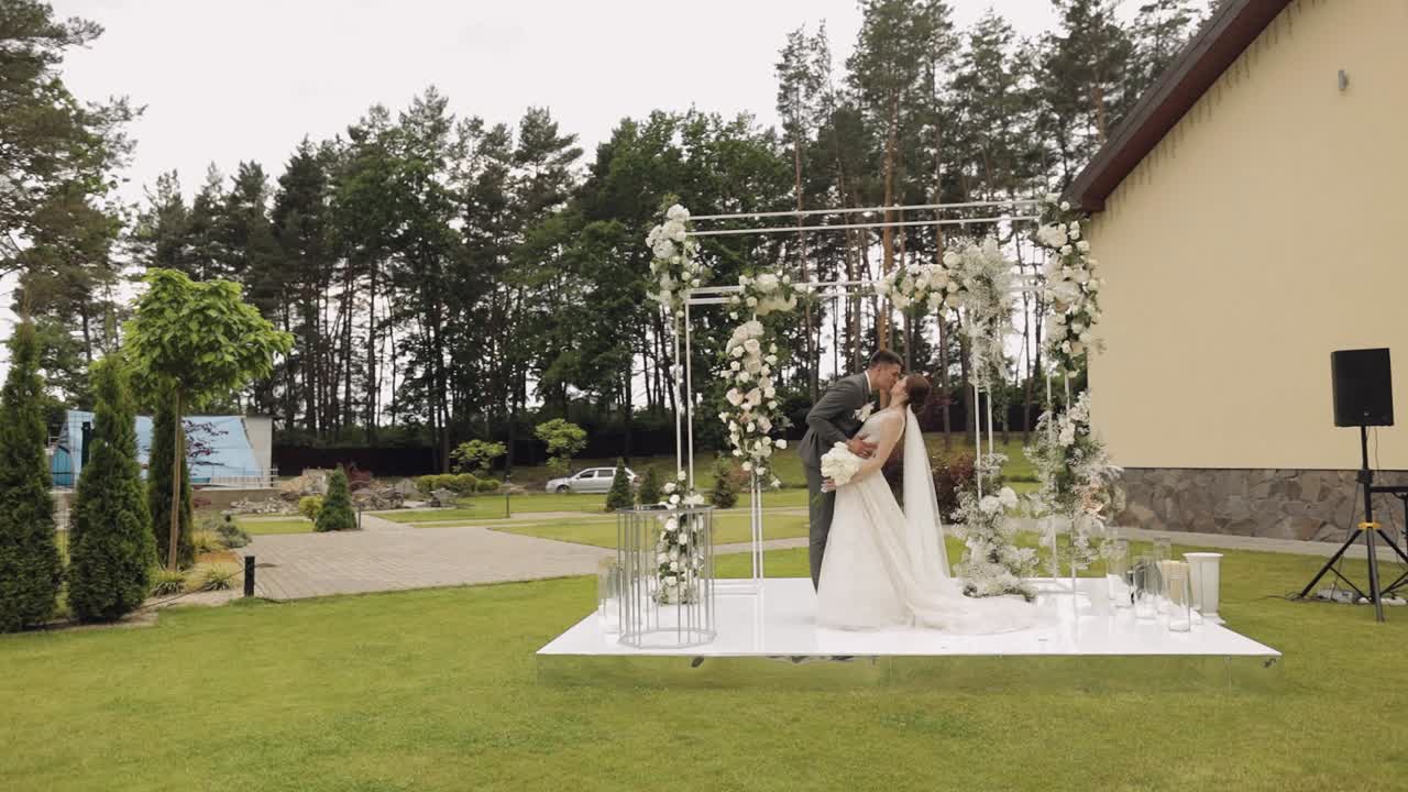 novia y novio besándose bajo un arco de flores en su ceremonia de boda al aire libre