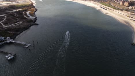 a high angle, aerial view of a boat heading out to sea in the east rockaway inlet in queens, ny on a sunny day