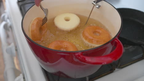 hand flips donuts with fork deep frying in pot, slow motion closeup