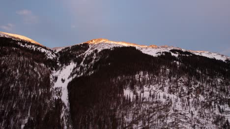 sunset hitting the peak of a snow covered mountain during golden hour