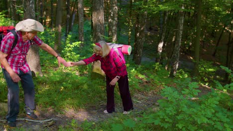 una mujer mayor en un viaje de aventura de senderismo sosteniendo la mano de un hombre ayudándola a escalar una colina de montaña en el bosque