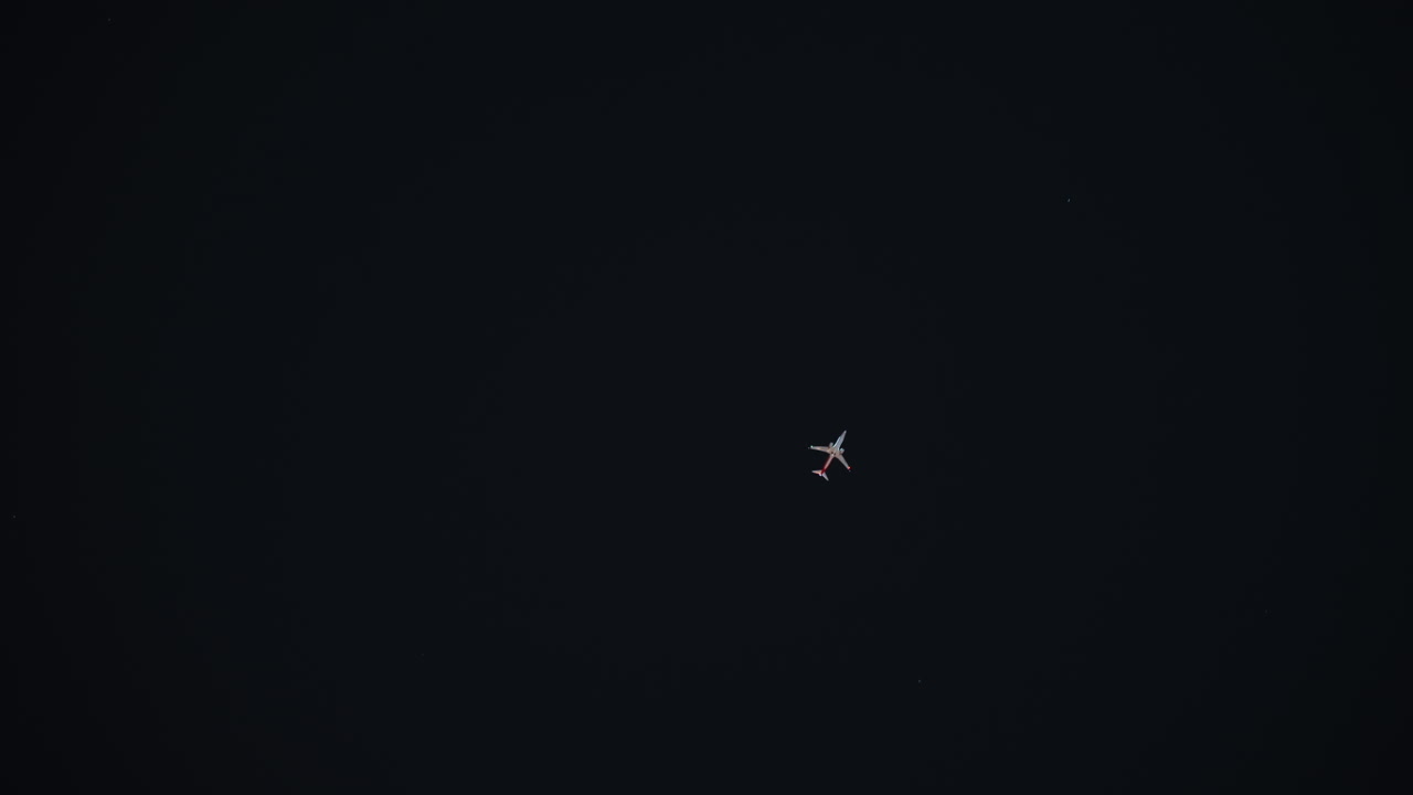 Piccolo aereo contro un cielo nero, piccolo velivolo luminescente centrato in un vasto spazio negativo, sottili luci di navigazione, solitudine ad alta quota, minimalismo cinematografico, lenta deriva attraverso l'inquadratura, evocativo