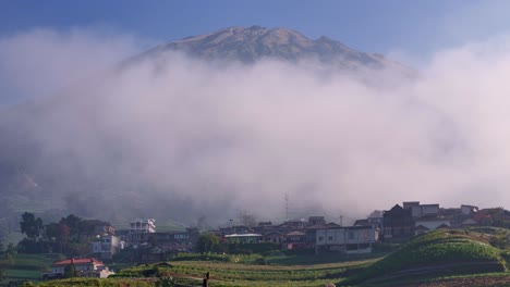 Fog rolling over a rural settlement at the foothills of a tall mountain on a clear blue sky day