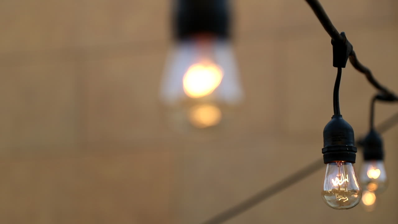 Vintage trendy light bulbs hang swaying in the wind outdoors in the open during an afternoon