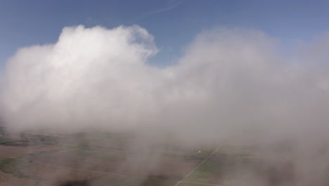 aerial drone moves through clouds above grassland and farmland in midwest of united states