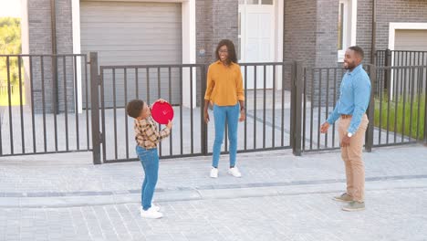 padres afroamericanos jugando al frisbee con un hijo pequeño y lindo al aire libre en la casa en las afueras